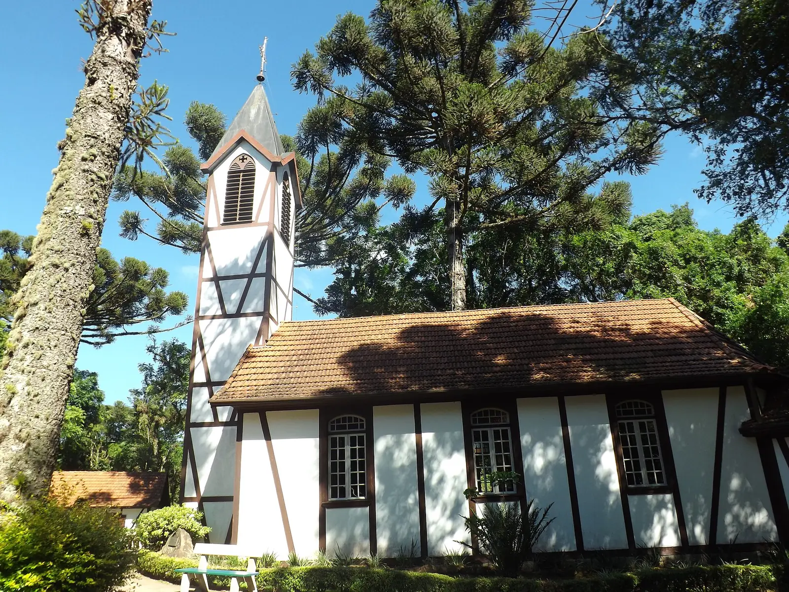 Capela em enxaimel, com torre, entre araucárias no Parque Aldeia do Imigrante