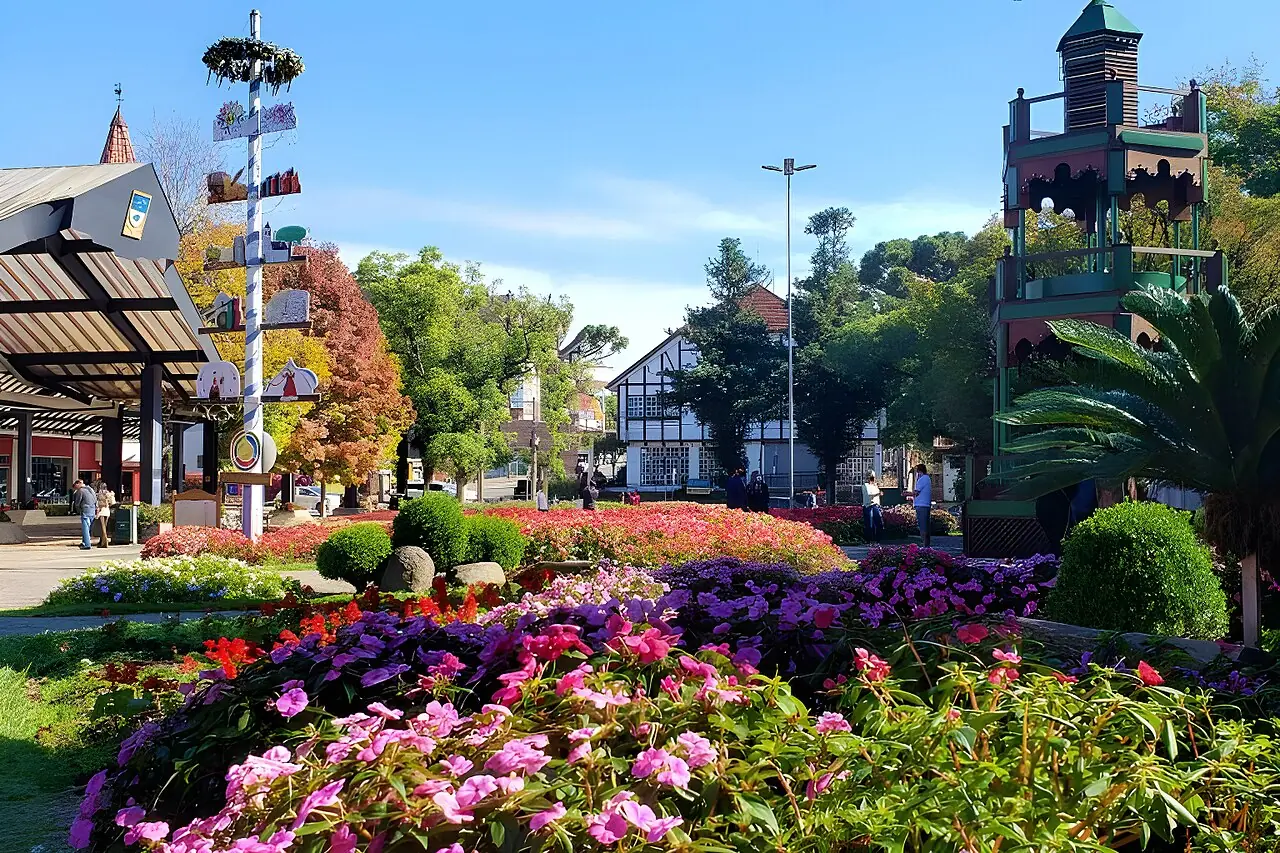 Canteiros floridos no centro de Nova Petrópolis, com um mastro decorado e casas em estilo enxaimel ao fundo