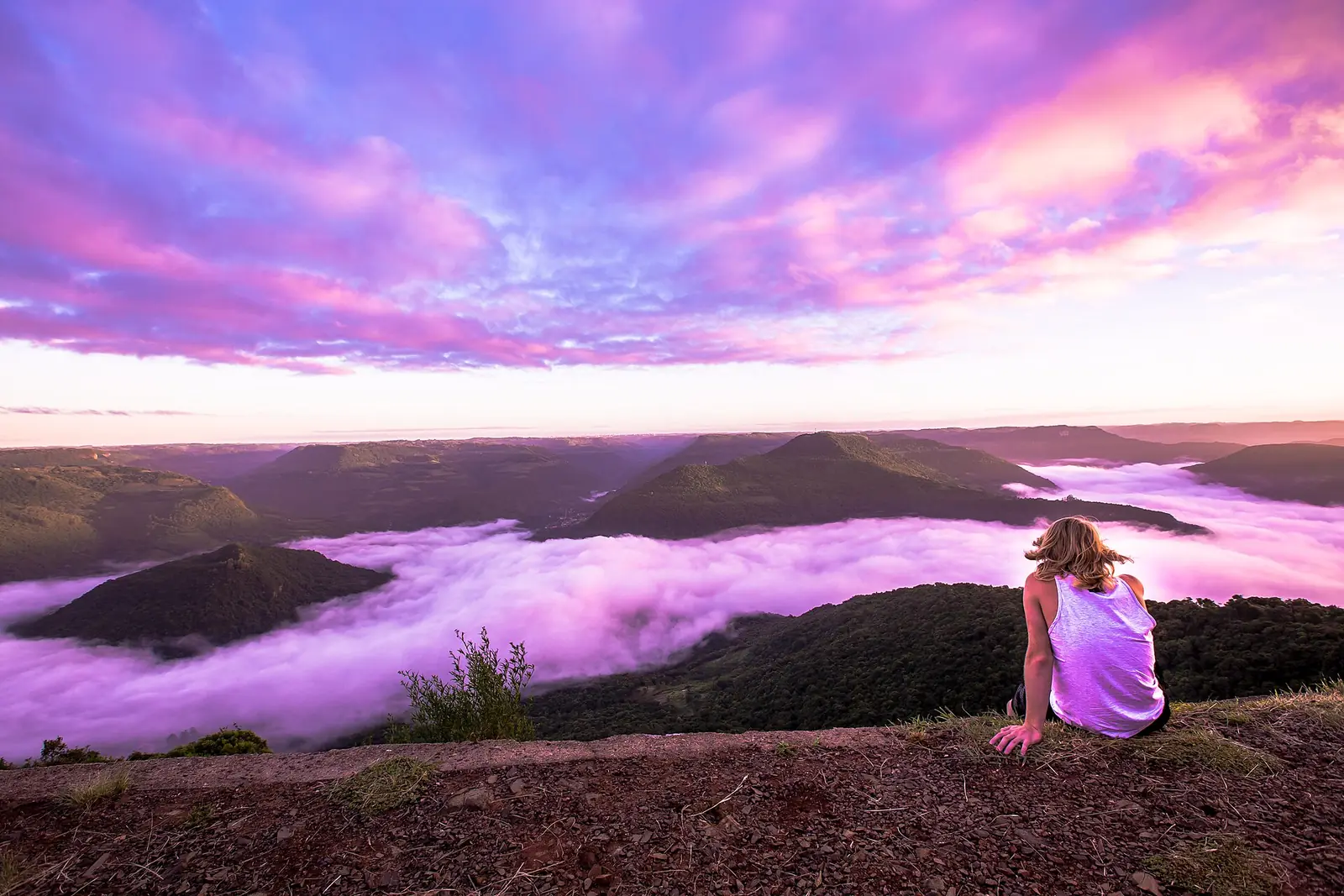 Amanhecer no Ninho das Águias, com neblina sobre o vale e uma pessoa sentada de costas
